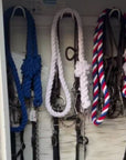 Ravenox red, white, and blue twisted cotton horse leads with chain and snap, hung in a barn alongside leather halters for horses. (1806013268058)