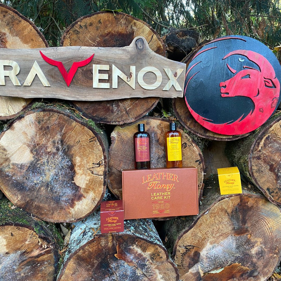 A rustic wood pile featuring a collection of Leather Honey leather care products alongside the Ravenox logo. (8289574846701)