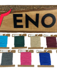 Array of Ravenox Cotton Macrame Cords in 2mm & 3mm sizes, showcased in an array of colors on cardboard disks, set against a custom wooden Ravenox sign. (7469797376237) (8431823257837)